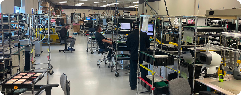 Trane Commercial HVAC Controls facility interior showing workers at workstations with metal shelving and equipment